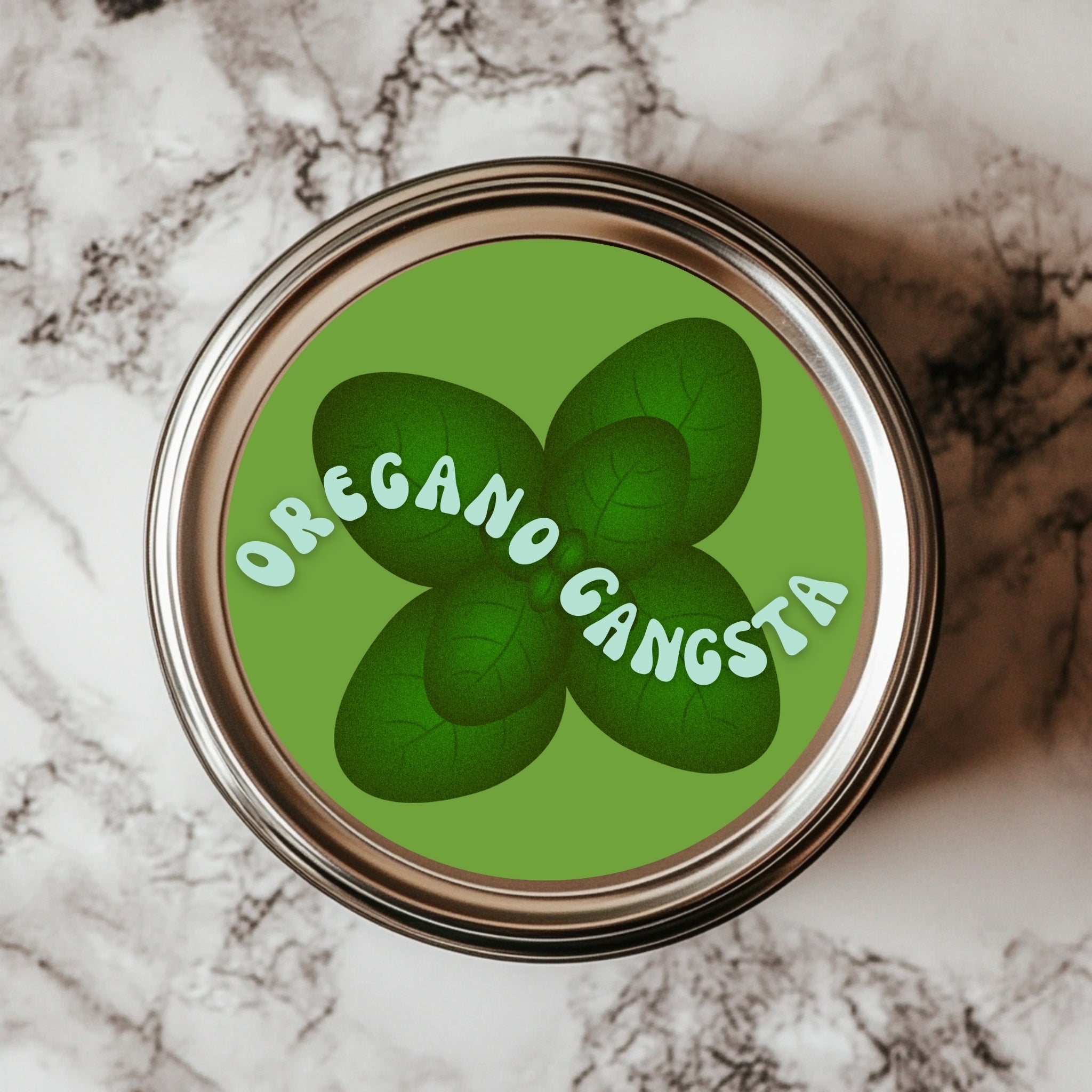 A round sticker with a green background featuring the text 'OREGANO GANGSTA' arranged around a cluster of oregano leaves on a marble surface.