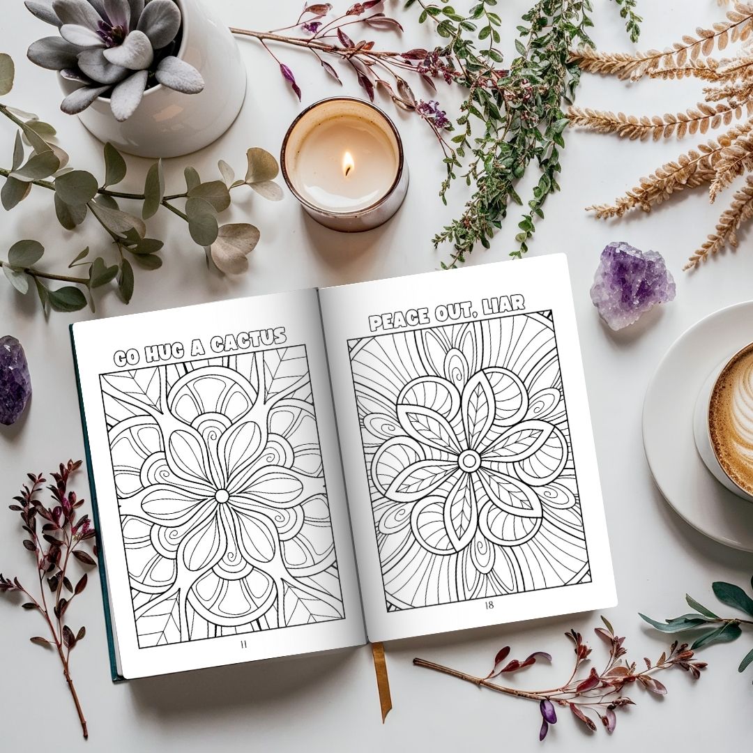 Coloring book open to pages with floral designs on a table with candles, plants, and coffee.