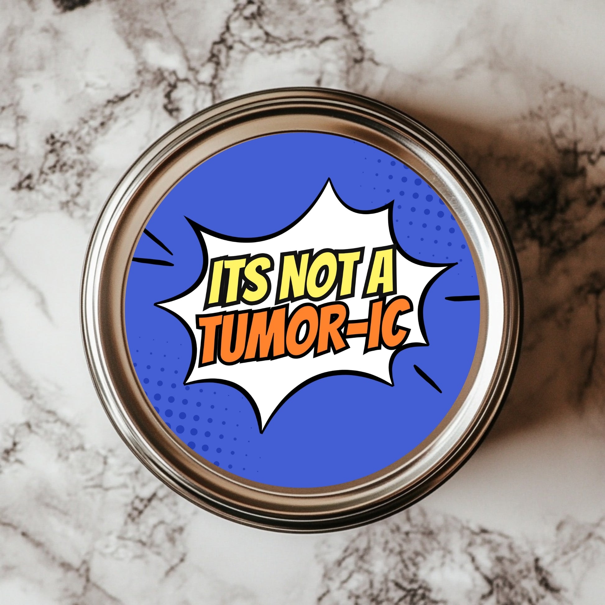 A round sticker with a comic book style that reads 'IT'S NOT A TUMOR-IC' in bold letters, placed on a marble surface.
