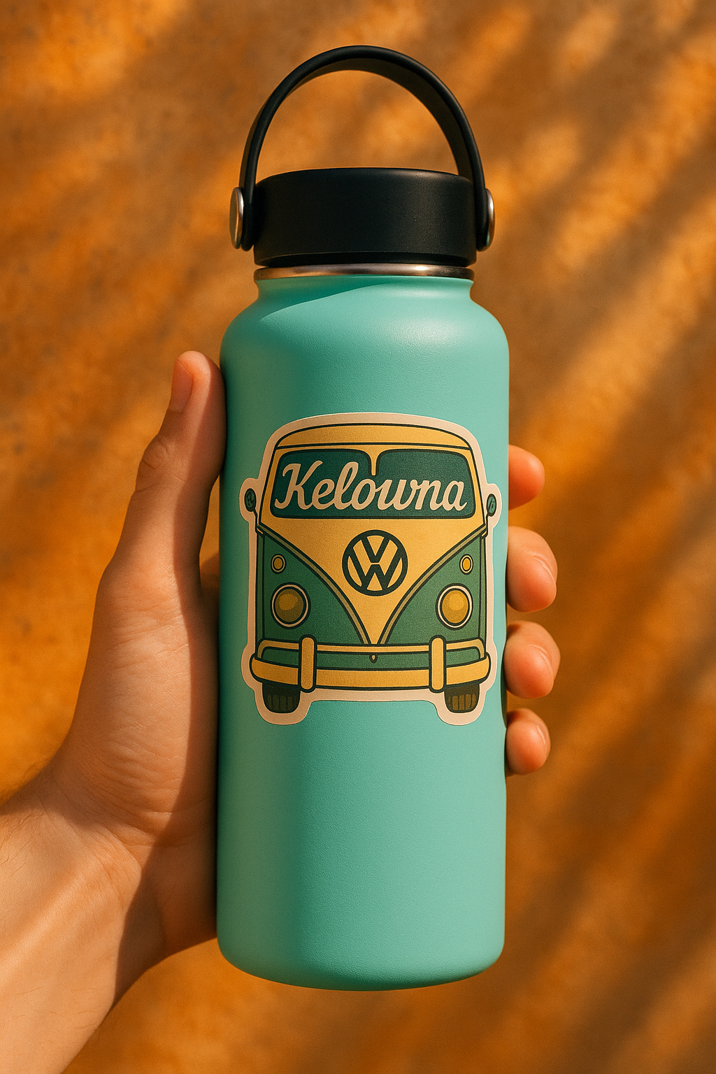 Teal water bottle with 'Kelowna' and Volkswagen logo held by a hand against a wooden background