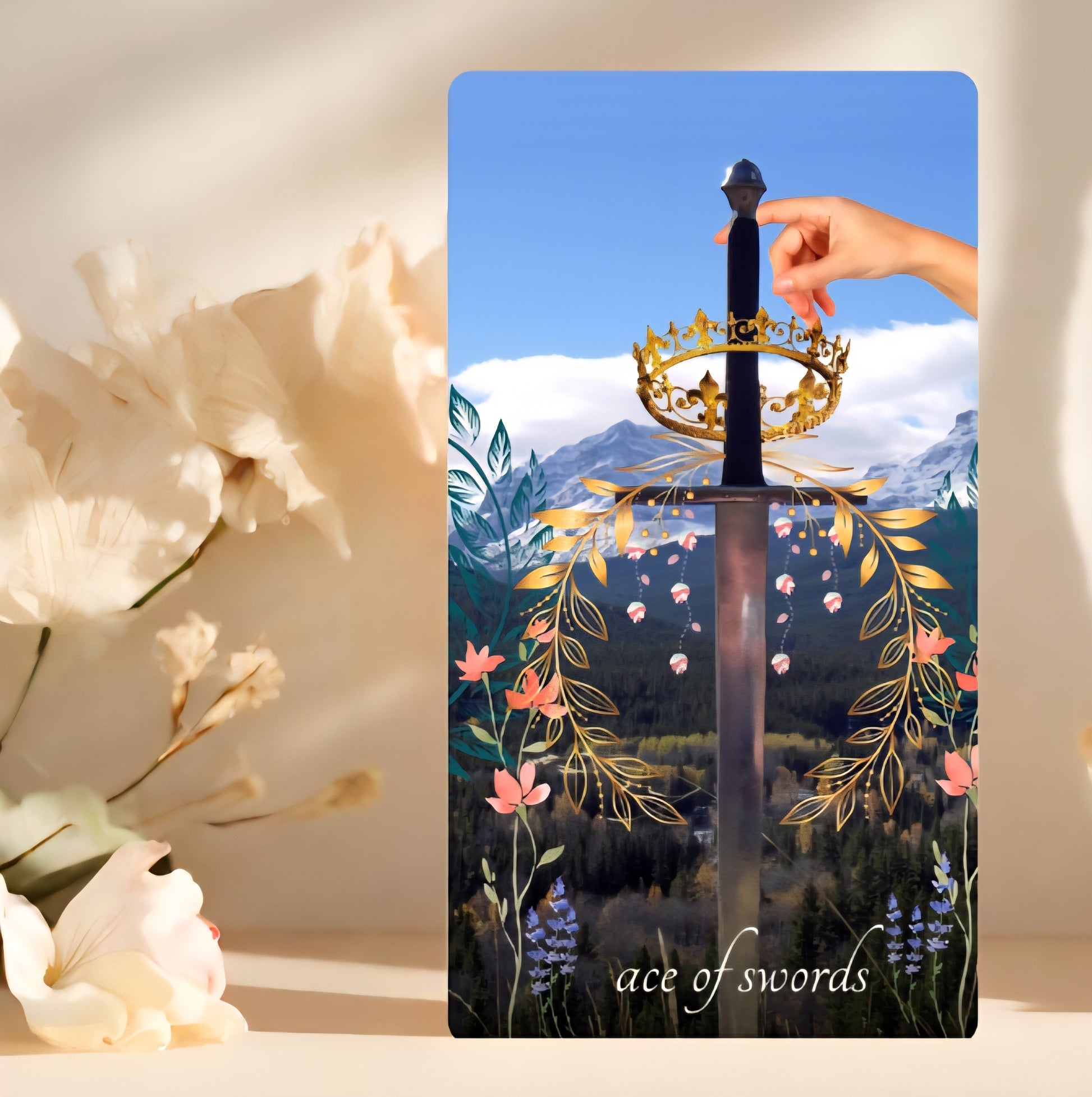 Card featuring a sword with a crown and floral design, labeled 'ace of swords', with flowers in the foreground.