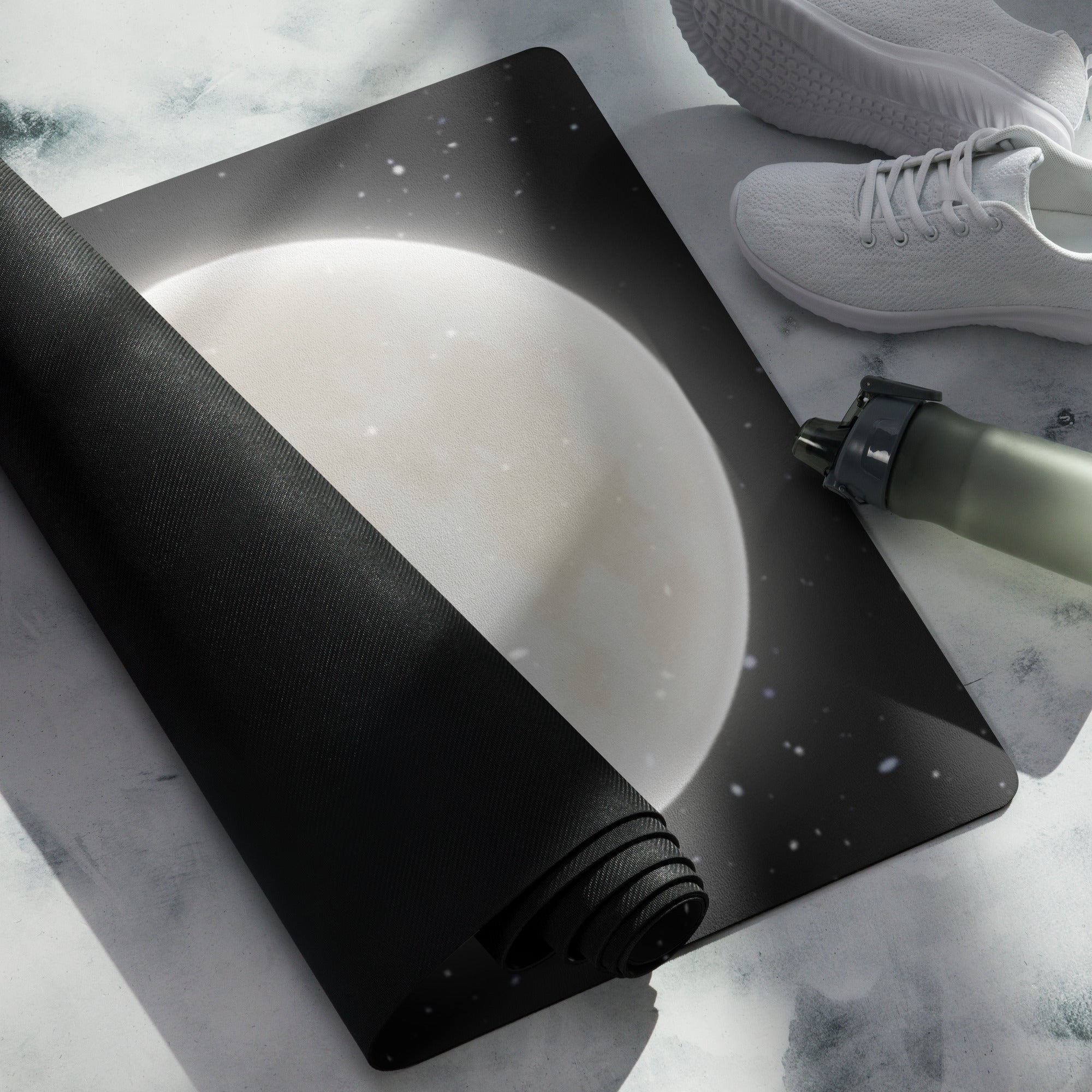 A yoga mat with a design of the moon and stars on it, rolled out next to a pair of white sneakers and a cylindrical object (presumably a pump).