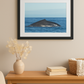 Framed picture of a whale in the ocean on a wall above a wooden table with decor items.
